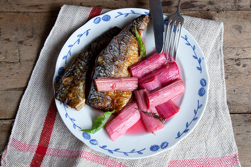 Gebakken makreel met rabarber op een bord, met mes en vork.